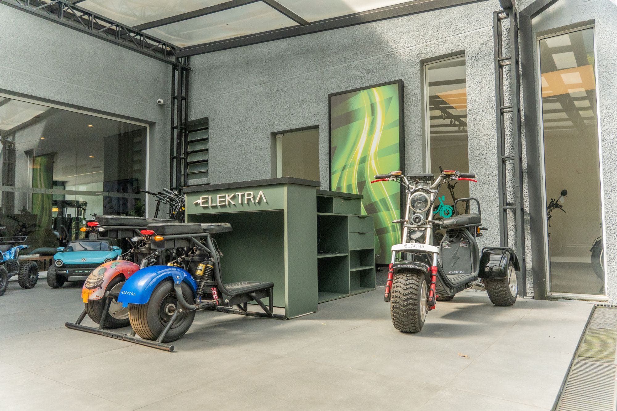 Recepção da Elektra, com balcão verde e scooters elétricos no pátio coberto