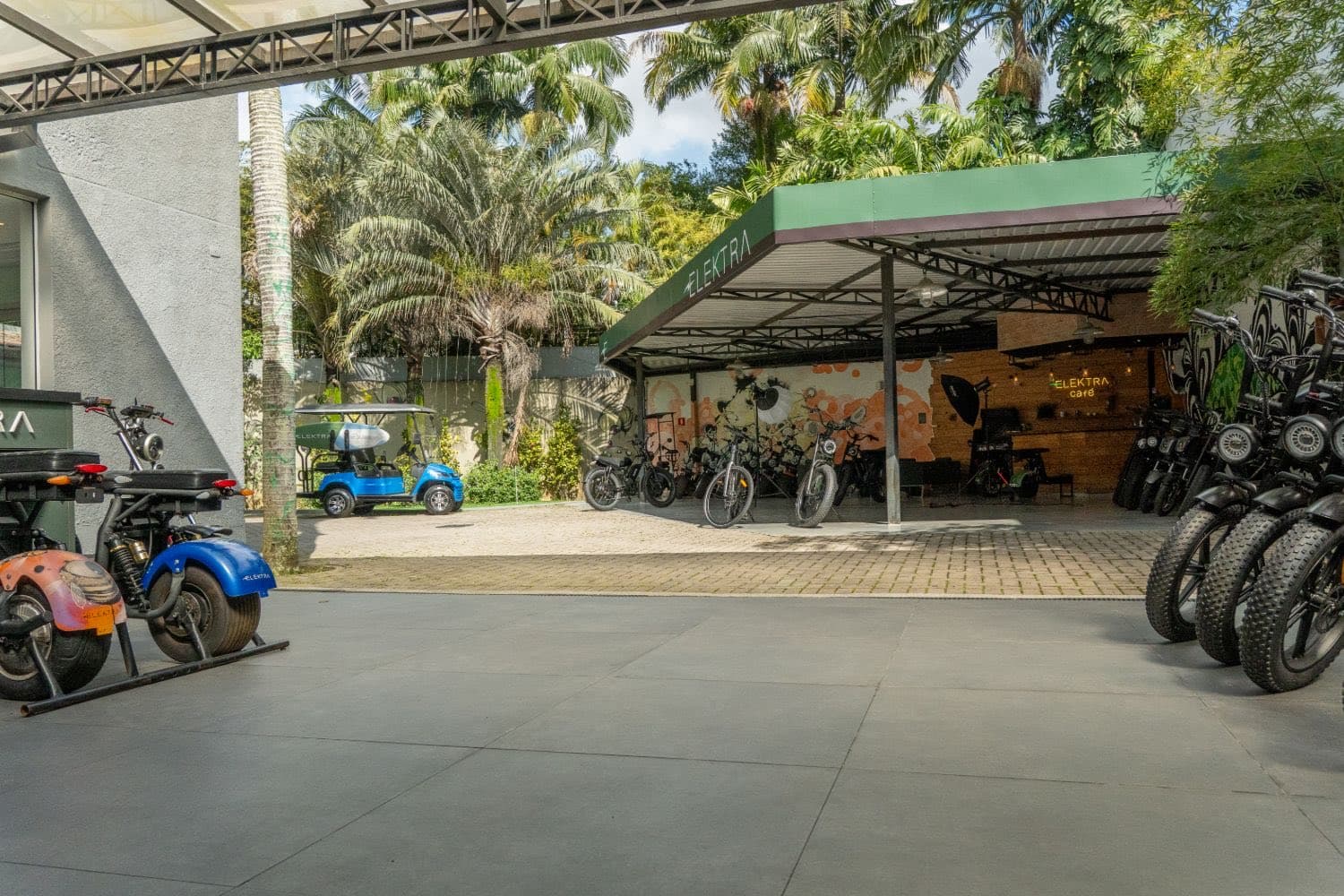 Pátio coberto da Elektra com bicicletas elétricas expostas, o Elektra Café ao fundo e um carrinho de golfe elétrico azul