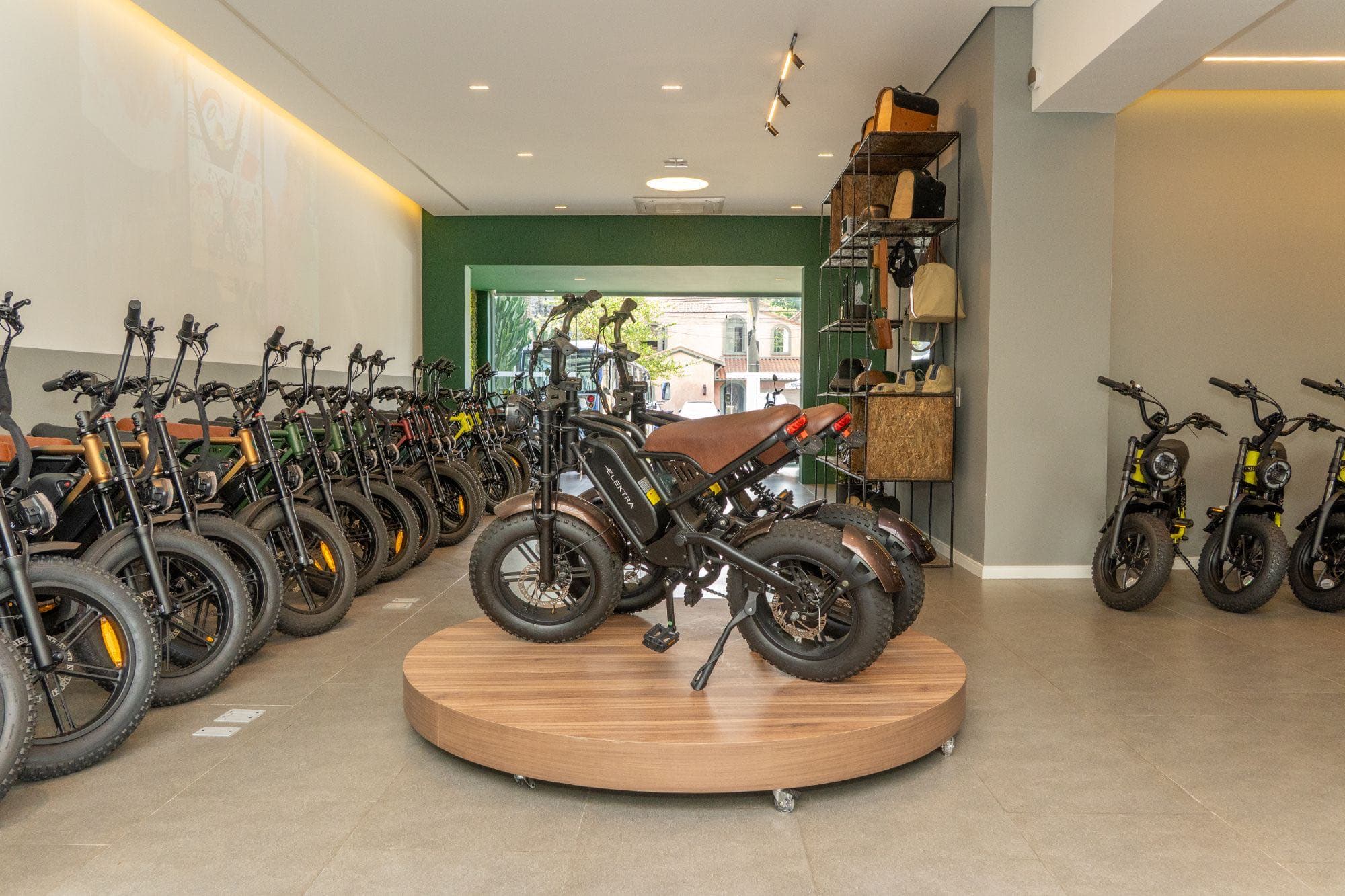 Bicicleta elétrica em plataforma circular de madeira no showroom, com outras bikes ao lado