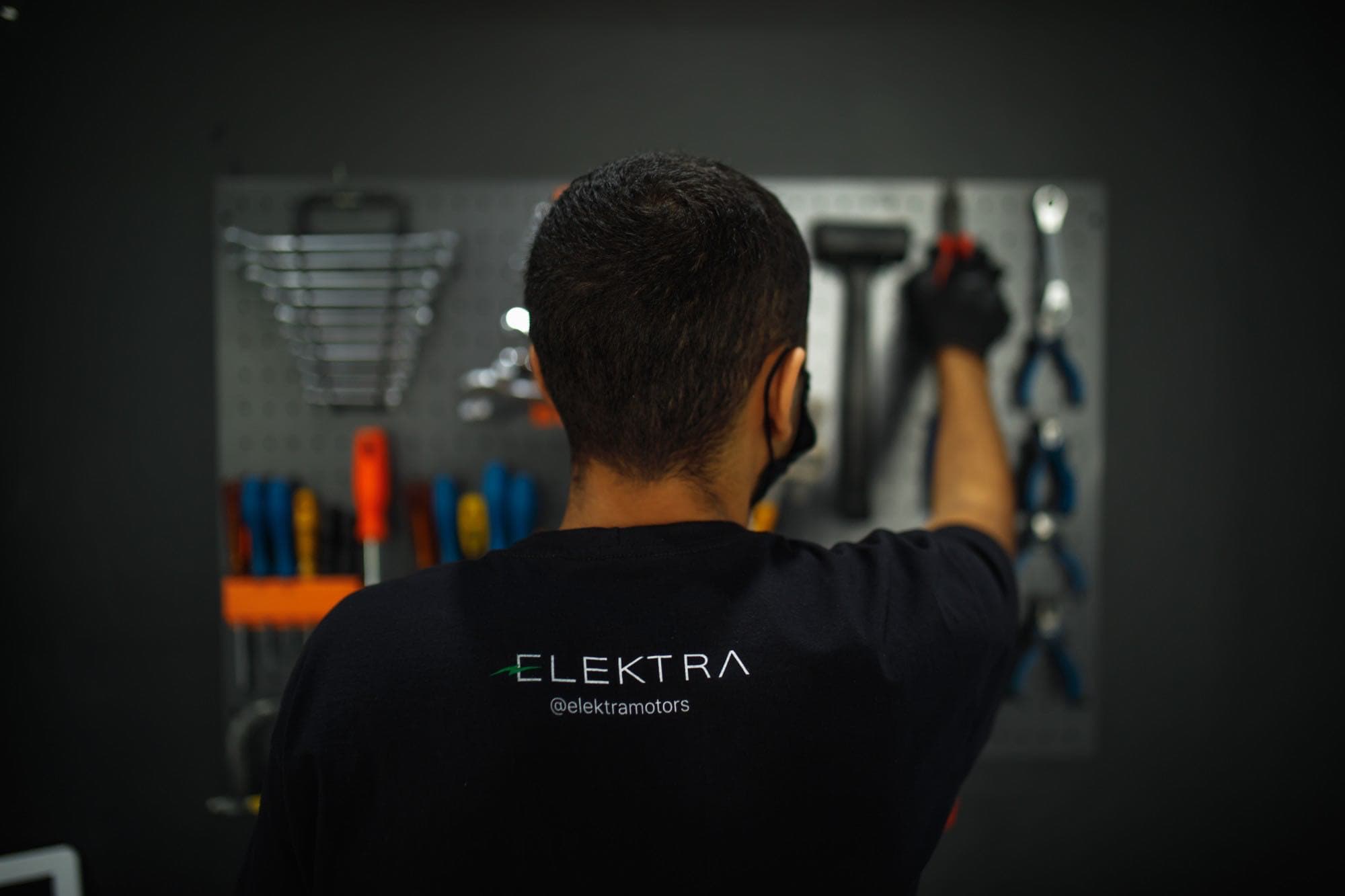 Técnico da Elektra de costas, com a camiseta da marca, pegando uma ferramenta no painel da oficina